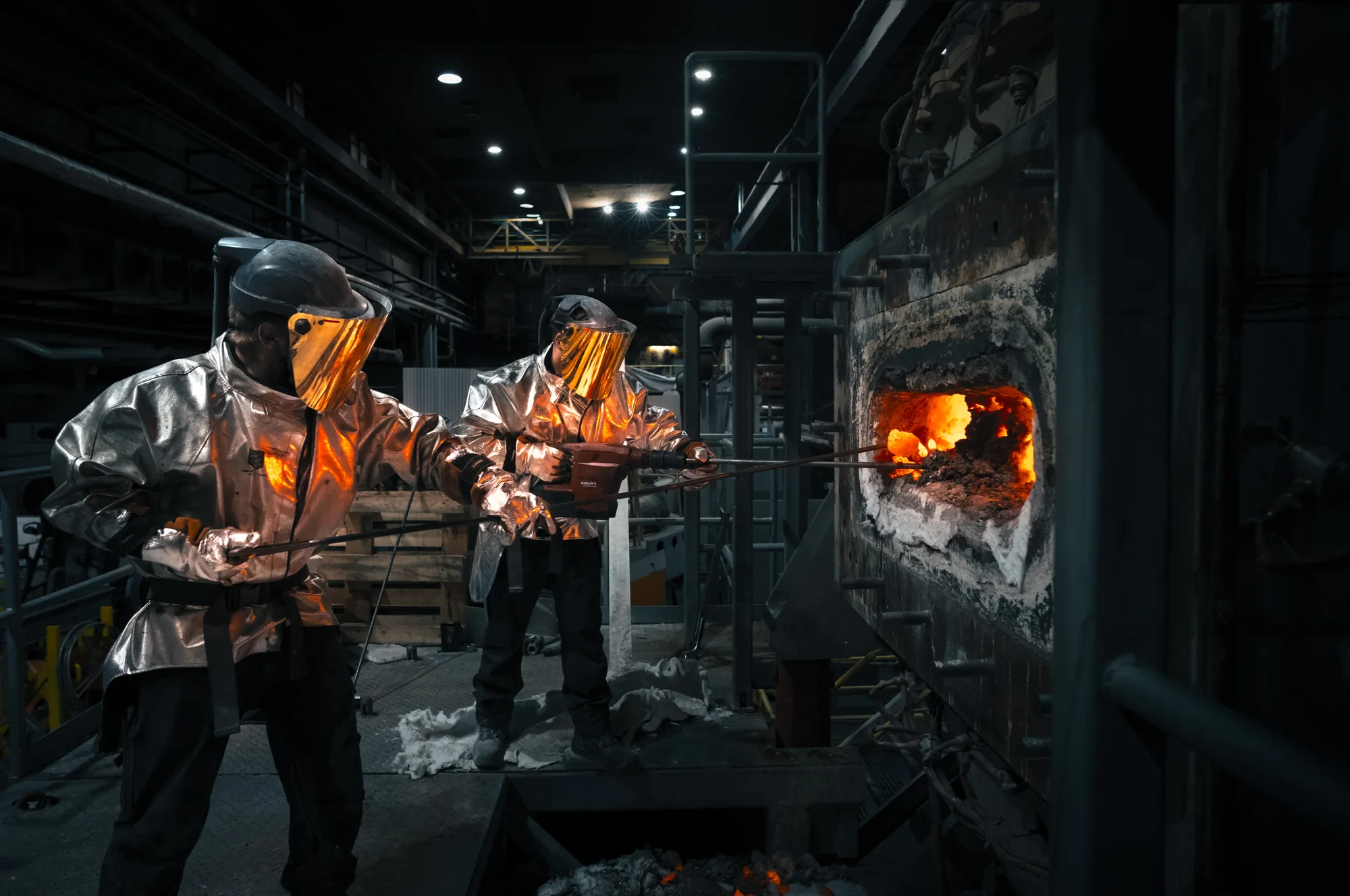 Dos fundidores con traje de protección aluminizado frente a la puerta de un horno, reportaje industrial para Calderys