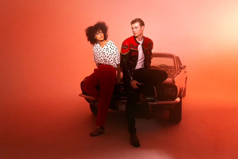Retrato de moda de una pareja sobre fondo rojo delante de un coche antiguo, sesión Leica
