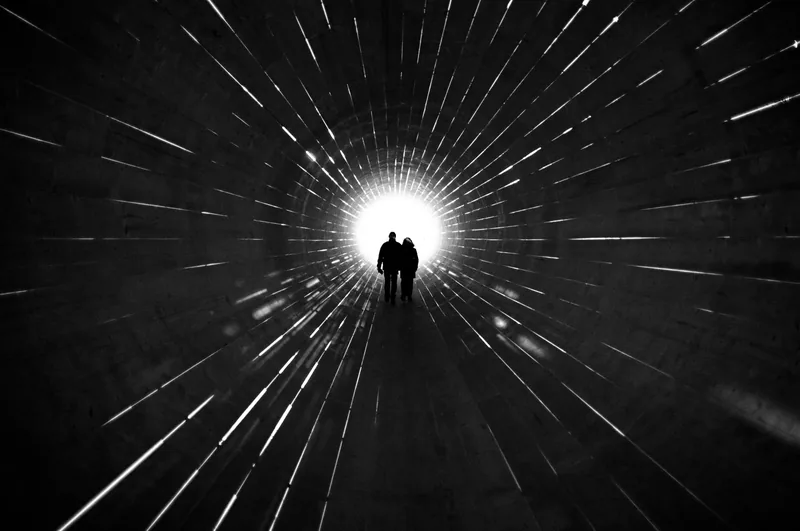 Two silhouettes at the end of a bright tunnel