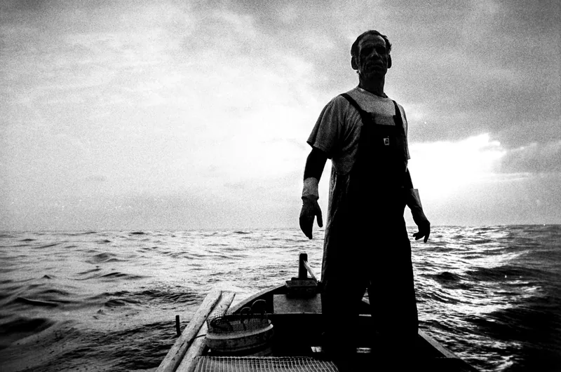 Fisherman standing in his boat facing the sea, black and white